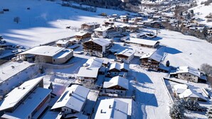 Un village enneigé, avec ses bâtiments traditionnels en bois, un télésiège et une chaîne de montagnes en arrière-plan.