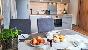 A compact kitchen with grey cabinets, a Bosch oven, and a dining area with a table set for breakfast. - Kragenjoch by Interhome (Wildschönau)