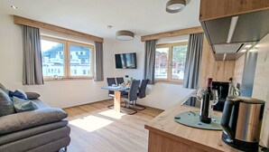 A modern living room with a sofa, dining table, and kitchen area with a sink and wine bottle. - Kragenjoch by Interhome (Wildschönau)