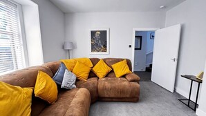Un salon moderne avec un canapé d’angle, une lampe et une œuvre d’art encadrée accrochée au mur.