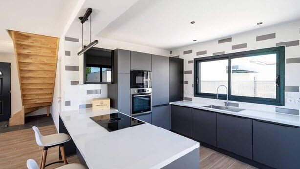 A modern kitchen with a central island, built-in appliances, and a large window providing natural light. - Maison Calypso de Narbonne (Narbonne)