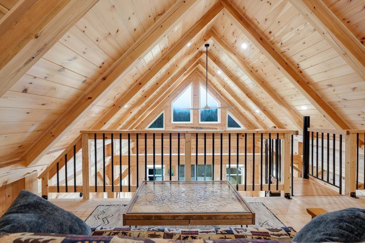 An attic bedroom with a sloped wooden ceiling, a bed, a window, and a view of the outside.