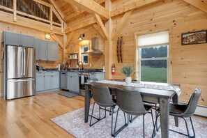 Interior de una cabaña de madera con cocina, comedor y ventanas amplias.