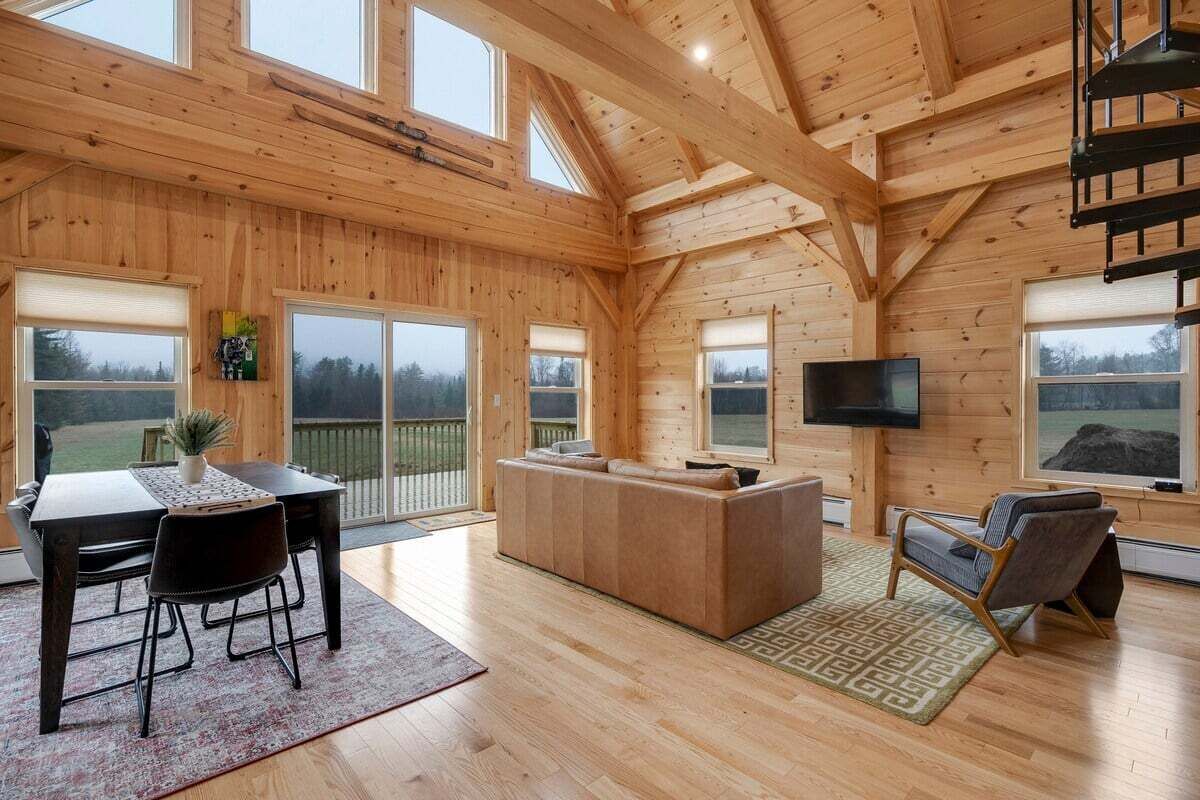 A spacious wooden interior with a dining area, sofa, TV, and a staircase.