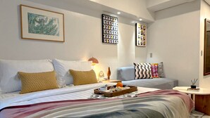 Ein modernes Hotelzimmer mit einem großen Bett, einer Couch und einem kleinen Tisch. An den Wänden befinden sich Bilderrahmen und auf dem Tisch steht eine Lampe.