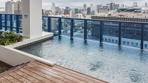 Ein Infinity-Pool auf dem Dach mit Blick auf die Stadt, umgeben von einer Holzterrasse und Glasgeländern.