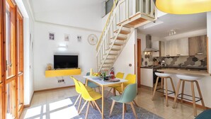 Una cocina moderna con estufa integrada, un comedor con sillas amarillas y una escalera que sube a un nivel superior.