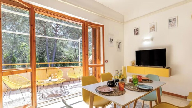 Comedor con una mesa preparada para cuatro, sillas amarillas y un televisor montado en la pared.