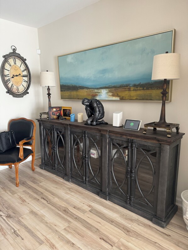 Un salón con una consola de madera oscura, un sillón de cuero negro, un cuadro de paisaje grande, un reloj antiguo y una lámpara.