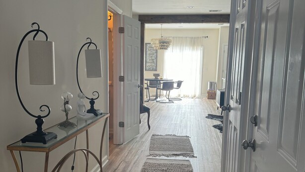 A hallway with a glass console table, two wall-mounted lamps, and a dining area with a table and chairs. - 3-bedroom Immaculate remodeled condo in marvelous Brentwood. (Brentwood)
