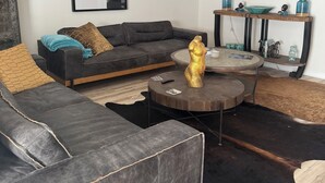A modern living room with a sectional sofa, a round coffee table, a chandelier, a mounted TV, and decorative items on a console table. - 3-bedroom Immaculate remodeled condo in marvelous Brentwood. (Brentwood)