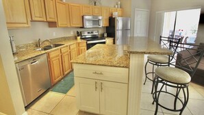 Una cocina con armarios de madera, electrodomésticos de acero inoxidable, encimeras de granito y una zona de bar con taburetes.