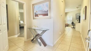 Un pasillo con una mesa de vidrio, un cuadro en la pared y una puerta que da a otra habitación.