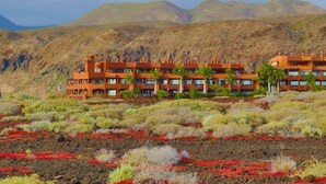 A hotel with multiple buildings, surrounded by a dry, hilly landscape with sparse vegetation. - Bahia - 2 bedroom seafront (Palm-Mar)