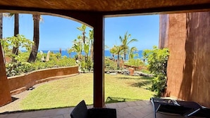 A covered outdoor seating area with wicker furniture, a view of a landscaped garden, and a clear blue sky. - Bahia - 2 bedroom seafront (Palm-Mar)