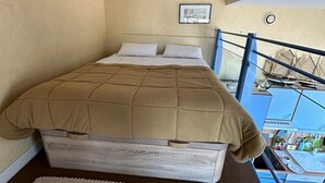 Une chambre à coucher avec un lit, un petit tapis, un tableau encadré au mur et un balcon avec une balustrade.