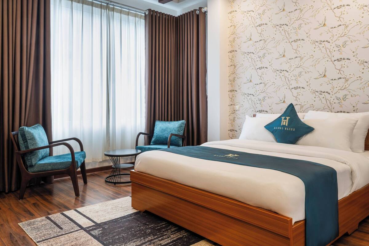 A hotel room with a large bed, two chairs, a small table, and a patterned wall.