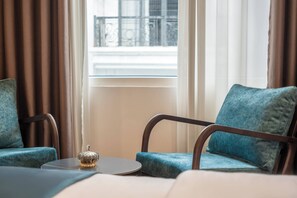 A room with two blue upholstered chairs, a small round table, and a window with curtains. - Hanoi Bliss Apartment Mai Hac De (Hanoi)