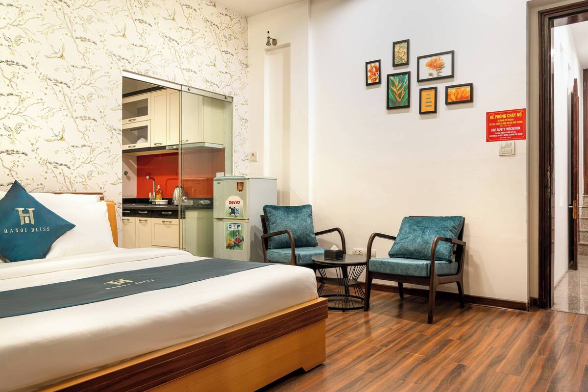 A hotel room with a bed, a kitchenette, a dining table, and two chairs.