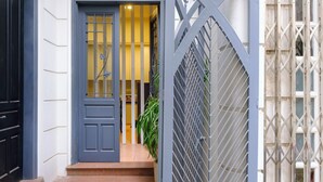 Een blauwe deur met een ruit, een trap die leidt naar een geel verlicht interieur, en een metalen poort met een geometrisch patroon.