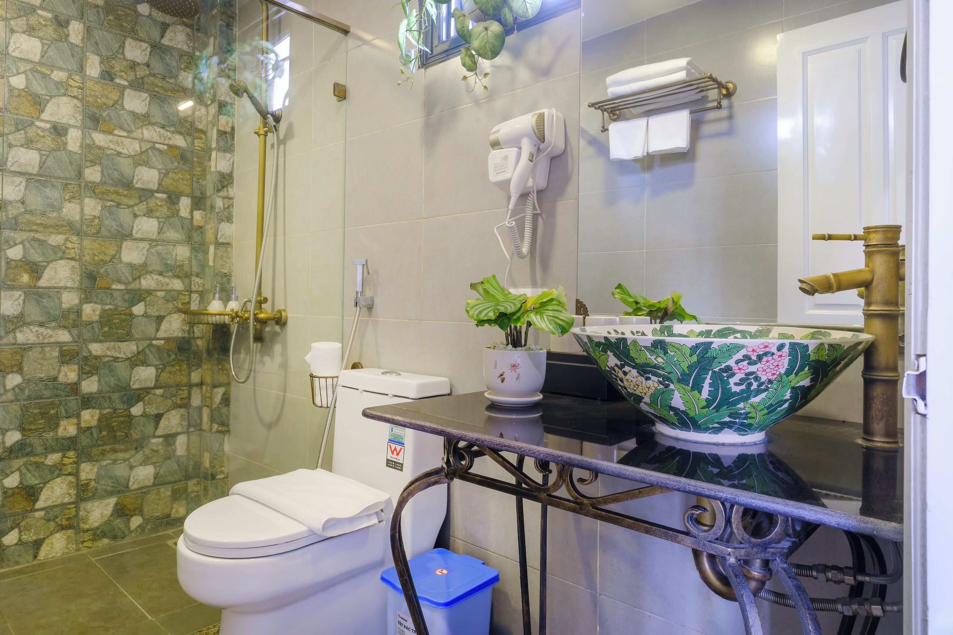 A bathroom with a stone shower wall, a toilet, a sink with a decorative bowl, and a towel rack.