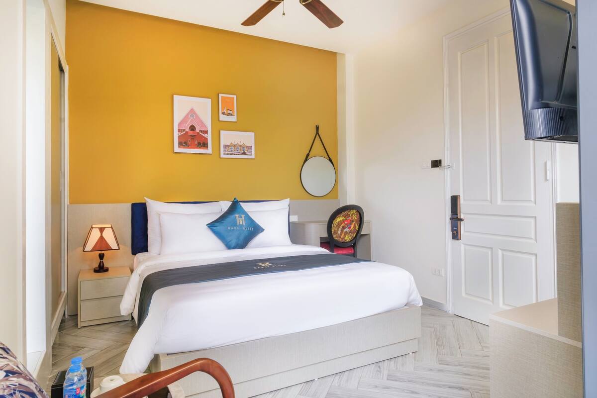 Une chambre d’hôtel avec un lit, une table de chevet, une lampe, un miroir et une porte.