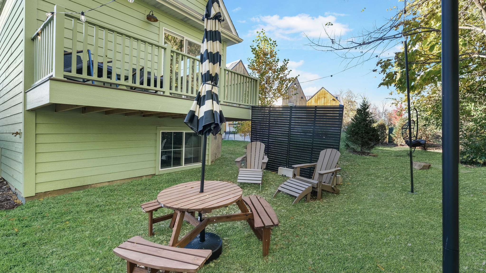 Un patio trasero con una terraza de madera, una mesa de picnic y dos sillas Adirondack.