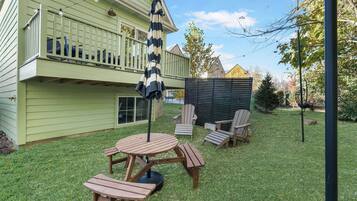 Un patio trasero con una terraza de madera, una mesa de picnic y dos sillas Adirondack.