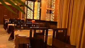 Un restaurant où les tables sont dressées pour le service, offrant une ambiance chaleureuse grâce à des décorations murales à motifs et un éclairage doux.