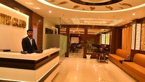 Un espace d’accueil d’hôtel au design moderne, comprenant un comptoir d’accueil, un coin salon et des éléments décoratifs au plafond.