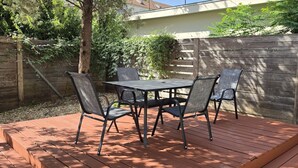 An outdoor patio with a table and four chairs, surrounded by a wooden deck and a wooden fence.