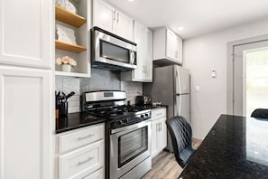 Una cocina moderna con armarios blancos, estufa de acero inoxidable, microondas y refrigerador.