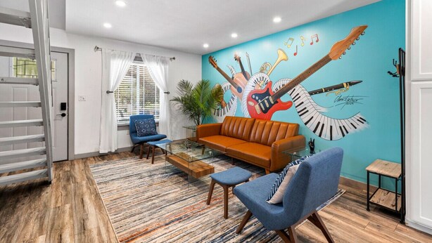 Sala de estar con un mural azul, un sofá marrón, sillas azules y una mesa de centro de vidrio.