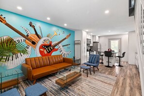 A modern living room with a mural of musical instruments, a brown leather sofa, a glass coffee table, and a blue armchair.