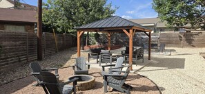 An outdoor patio area with a wooden pergola, seating arrangements, and a fire pit.
