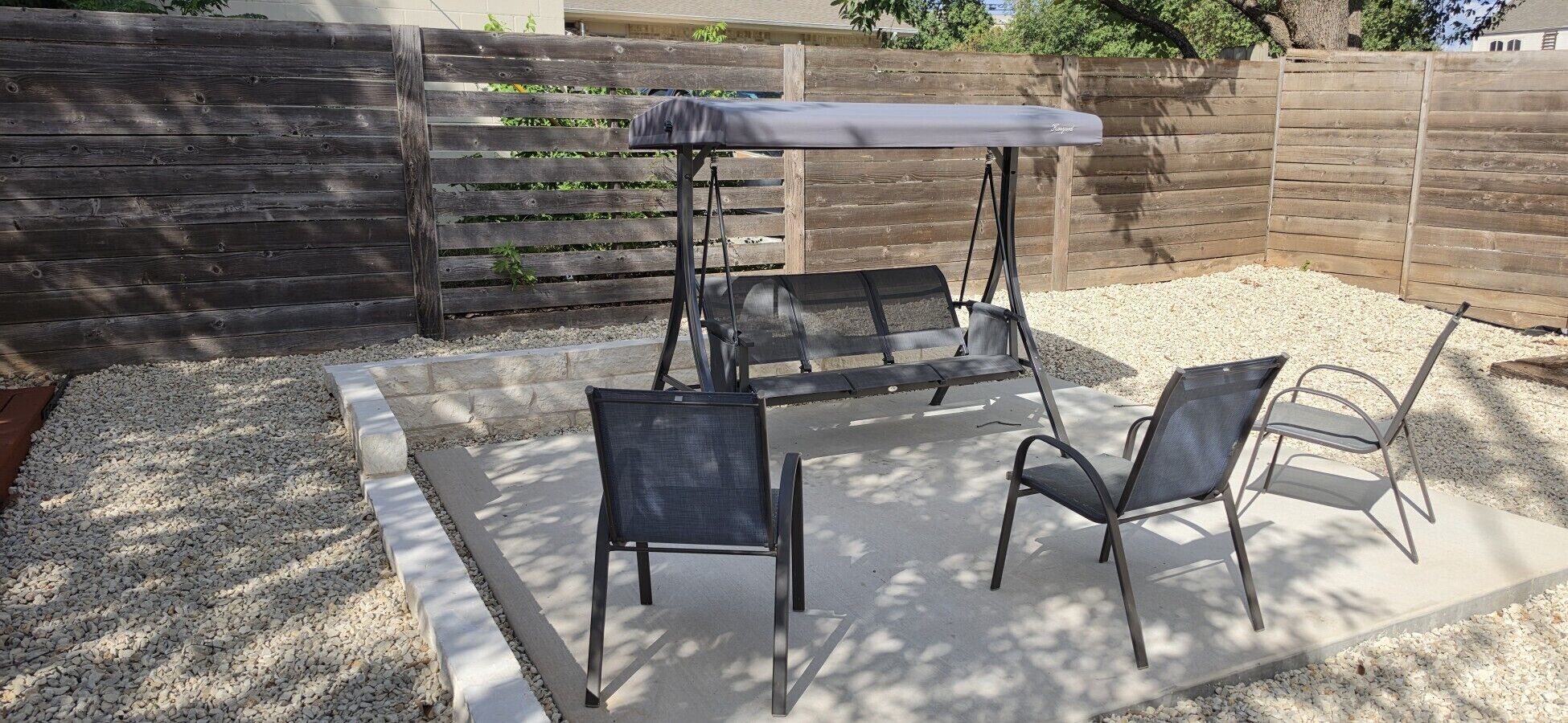 Un espace patio comprenant une balançoire, deux chaises et une table dotée d’un auvent.
