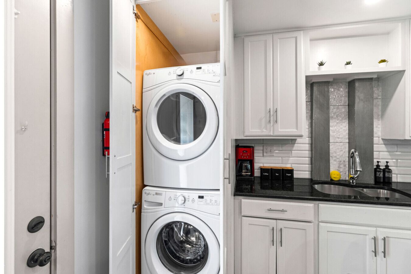 A compact laundry room with two stacked front-loading washing machines, a coffee maker, and a sink with a modern faucet.