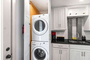 A compact laundry room with two stacked front-loading washing machines, a coffee maker, and a sink with a modern faucet.
