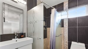 Un baño moderno con un lavamanos blanco, cabina de ducha de vidrio y un inodoro.