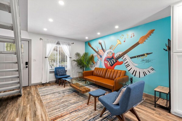 Een woonkamer met een blauwe muurschildering, een bruine bank, blauwe stoelen en een glazen salontafel.
