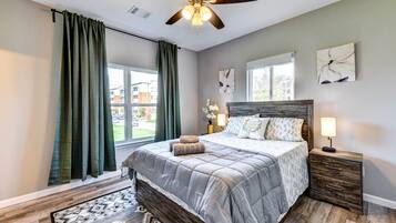 Une chambre à coucher avec un lit, des tables de chevet, un ventilateur de plafond et une fenêtre avec des rideaux.