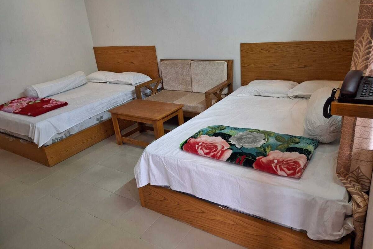 A room with two wooden beds, a small wooden table, and a telephone on a bedside table.