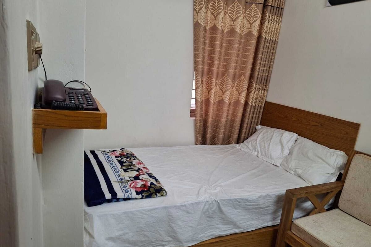 A single bed with a wooden headboard, a bedside table with a telephone, and a patterned throw blanket.