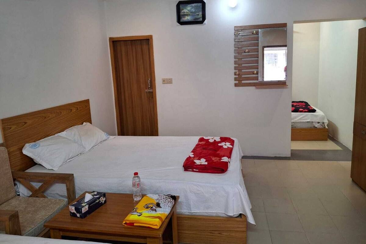 A hotel room with a wooden bed, a small table with a bottle and tissues, a mirror, and a door.