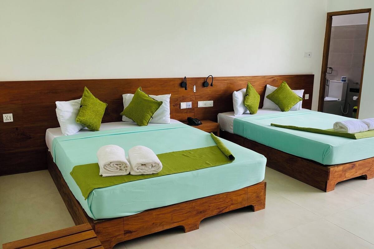 Twee eenpersoonsbedden met groene beddengoed, witte kussens en groene sierkussens. Elk bed heeft een houten hoofdbord en een klein nachtkastje met een telefoon.