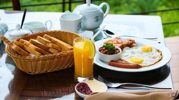 Ein Frühstückstisch mit Toast, Eiern, Würstchen und einem Glas Orangensaft, mit Blick auf eine grüne Landschaft.