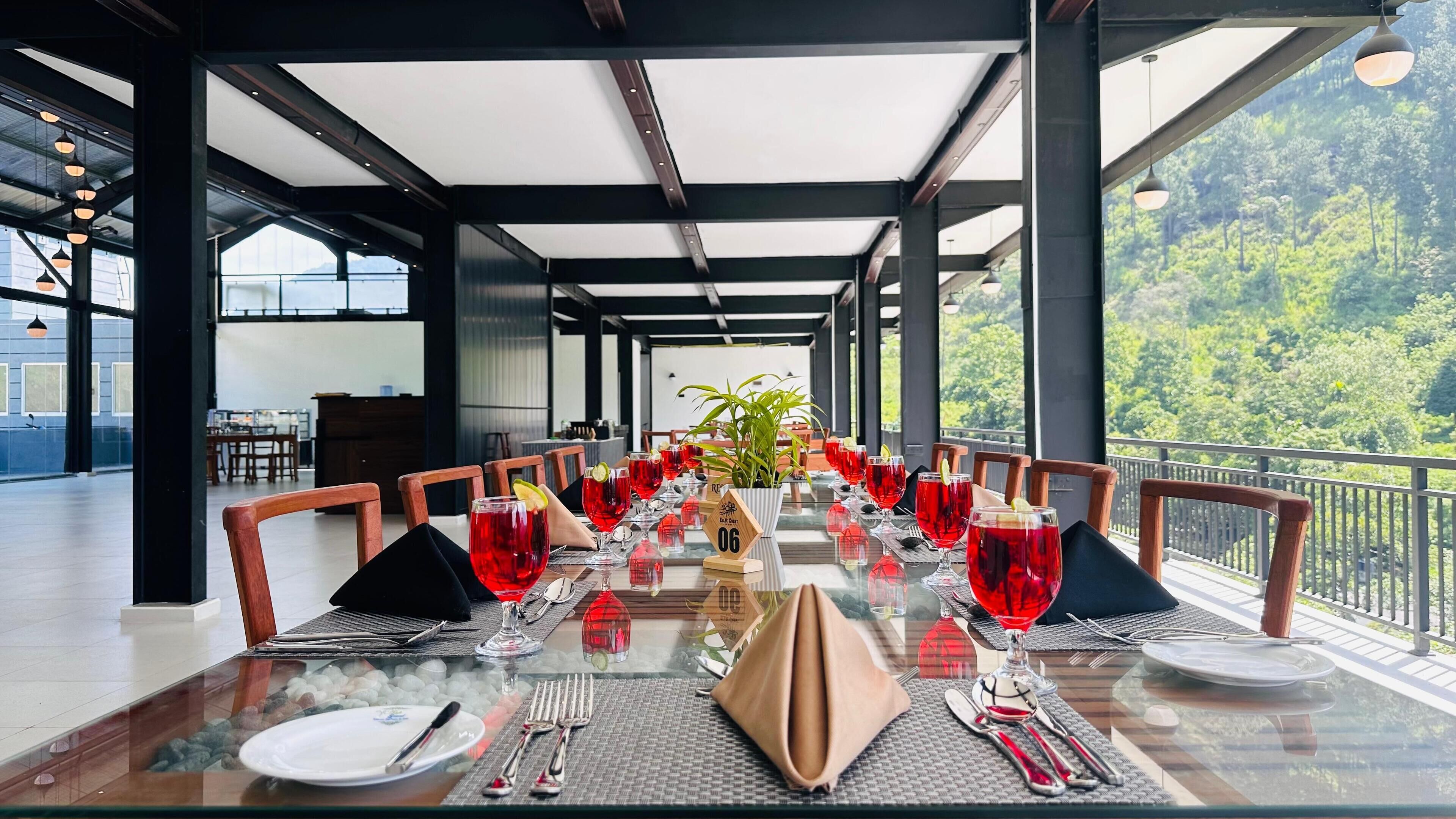 A table set for a meal with red drinks, a plant centerpiece, and a view of a forest.