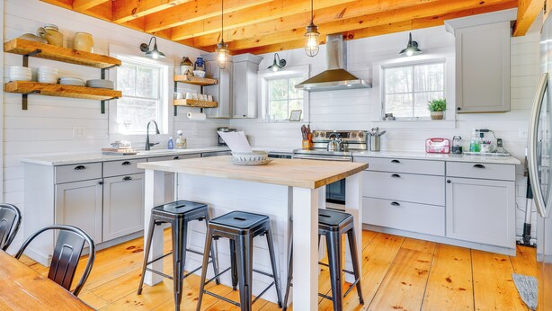 A modern kitchen with wooden beams, white cabinetry, and a central island with stools. - Paddle, Swim & Hike: Family Lake House in Vermont (Tinmouth)