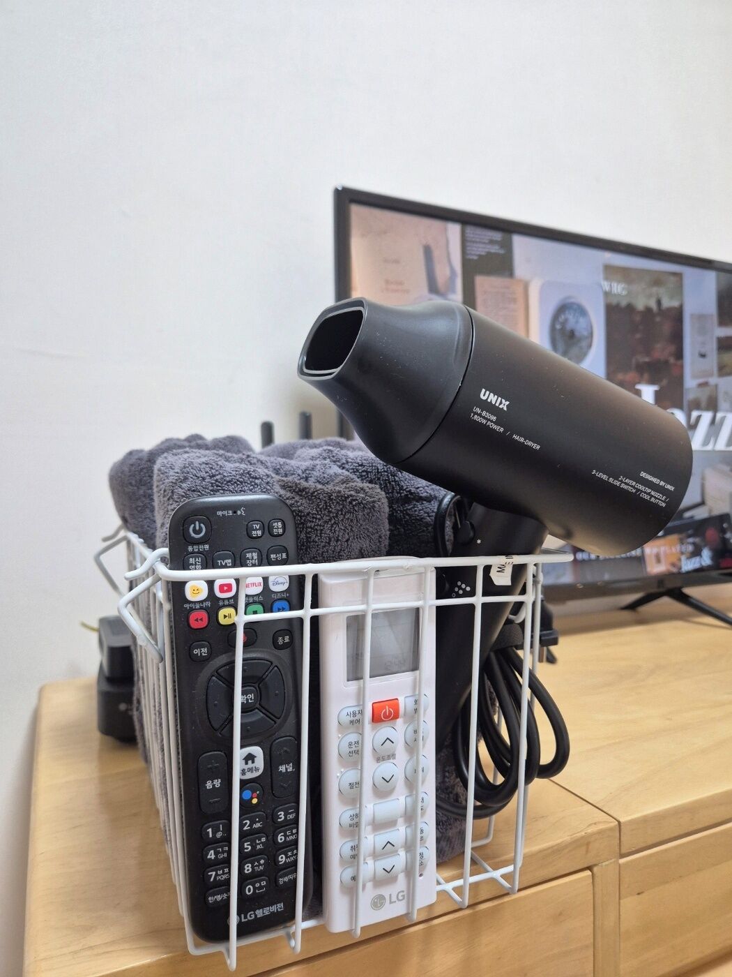 A remote control holder with multiple remotes, a hair dryer, and a television in the background.