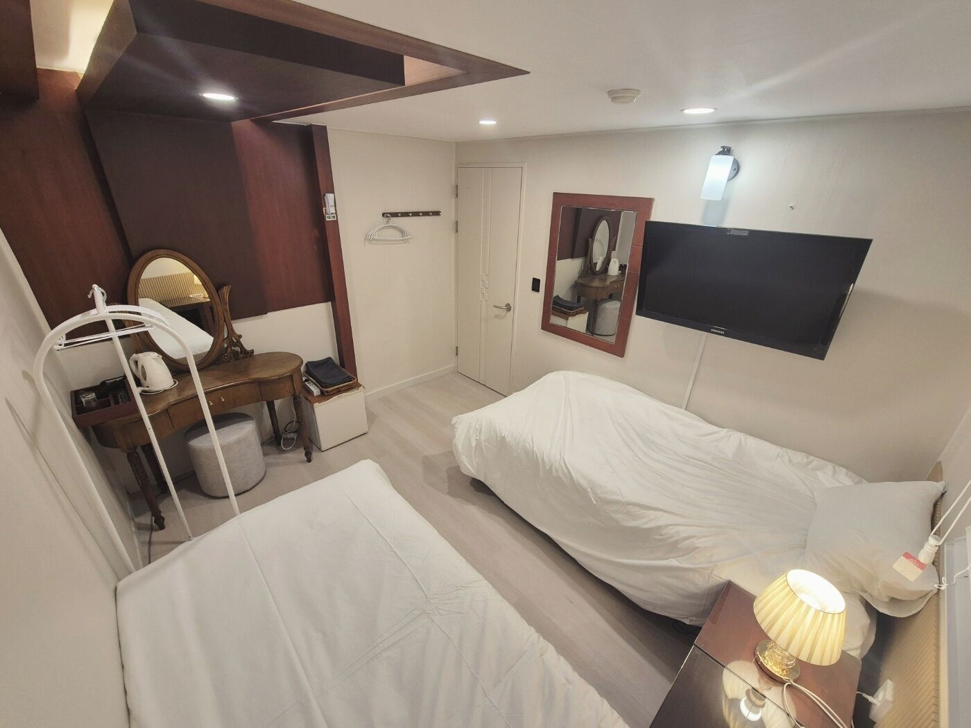 Habitación de hotel con cama, escritorio con silla, espejo, televisor y lámpara.